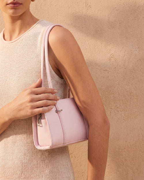 Model in a cream knit top carrying the Badr powder pink baguette bag against a sand-coloured wall – Nouva
