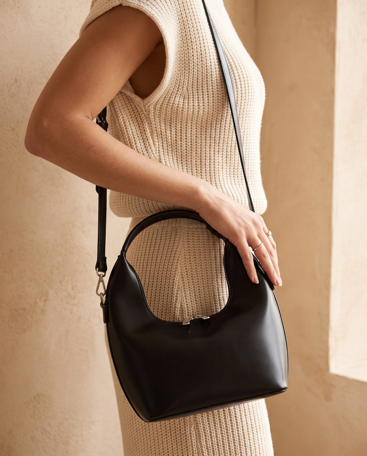 Model in a cream knit top with the Mizar black bucket bag on a long strap at her waist, compact 20 cm women's crossbody bag by Nouva